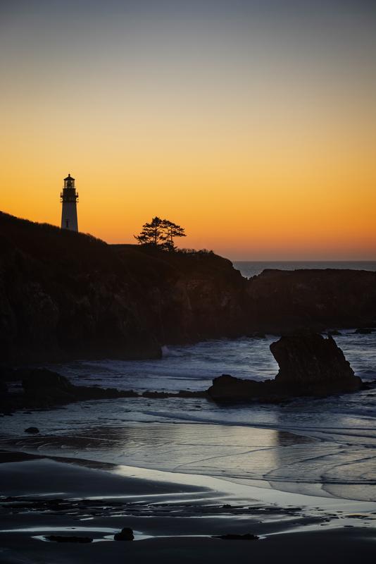 lighthouse overlooking orange sunset with rocks in the bay and ocean waves 