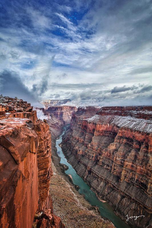 red rock canyon walls with massive drop and colorado river below with clouds art by eddie jongas