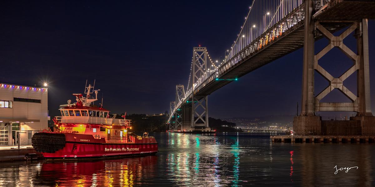 fireboat at night at bay next to bay bridge city lights